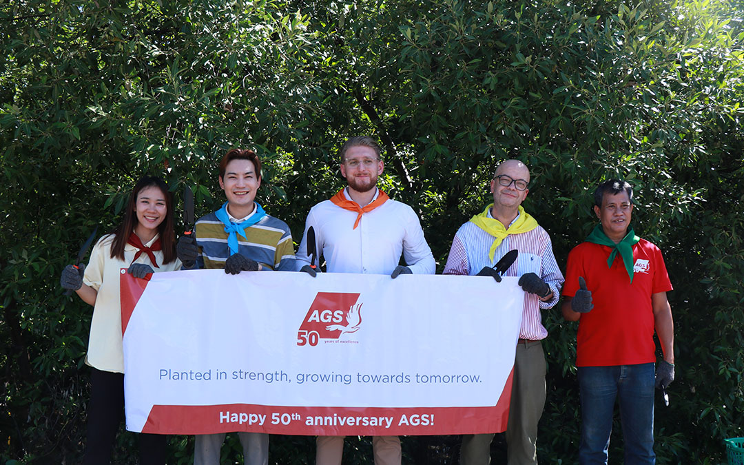 The AGS Thailand team holding a large "Happy 50th Birthday AGS!" banner to celebrate five decades of global excellence.